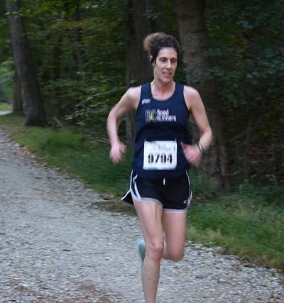 Janet Braunstein running on the C&O Towpath in a navy blue DC Road Runners singlet