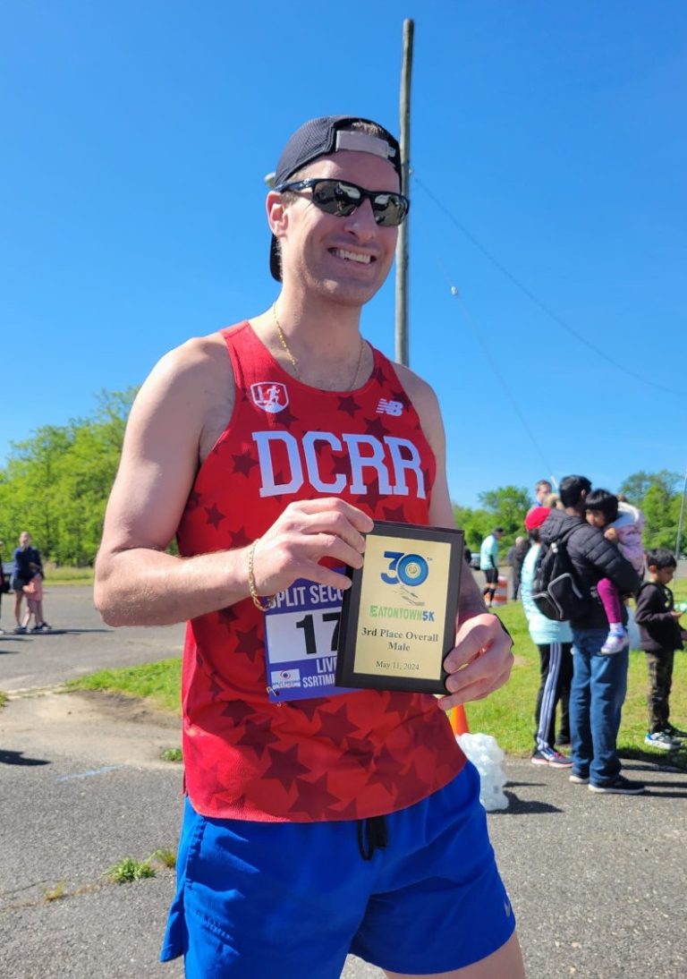 Joseph P Fisher holding a third place finisher's plaque while wearing a red DC Road Runners singlet and blue shorts