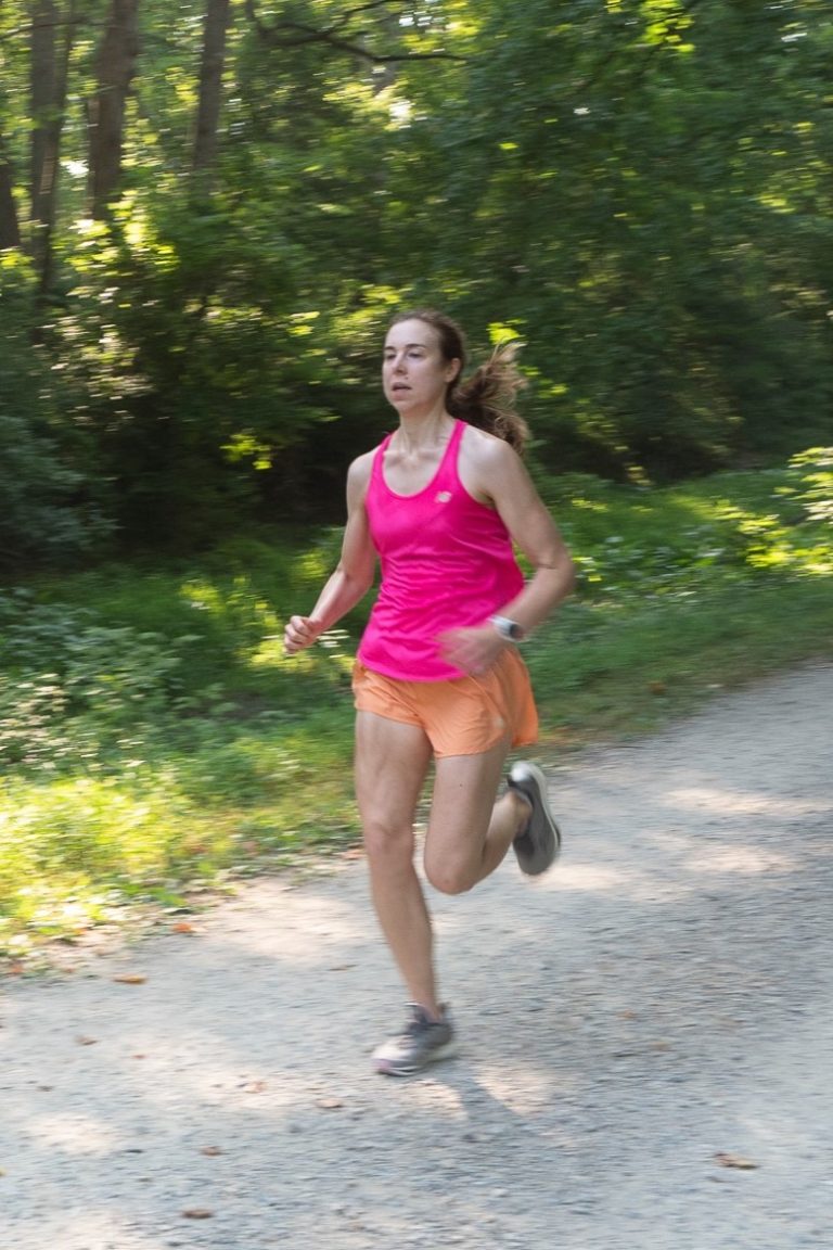 Bonnie Peruski running on a dirt trail with green trees in the background