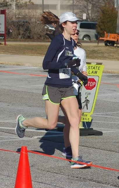 Bonnie Harvey running on a paved road wearing a navy blue DC Road Runners singlet