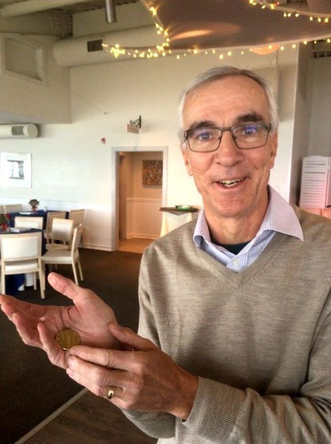 Ed Grant standing and holding in his palm a tiny gold medal won by American Johnny Hayes in the 1908 Olympic Marathon