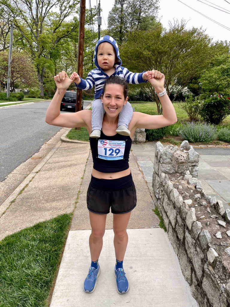 Gaither Smith holding her son on her shoulders while standing on the sidewalk, dressed in running gear