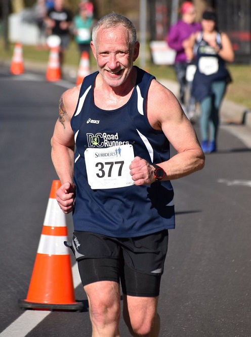 Keith Campbell running on a paved street wearing a navy blue DC Road Runners singlet