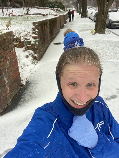 Kellie Honey wearing blue winter running gear standing on a snowy sidewalk taking a selfie