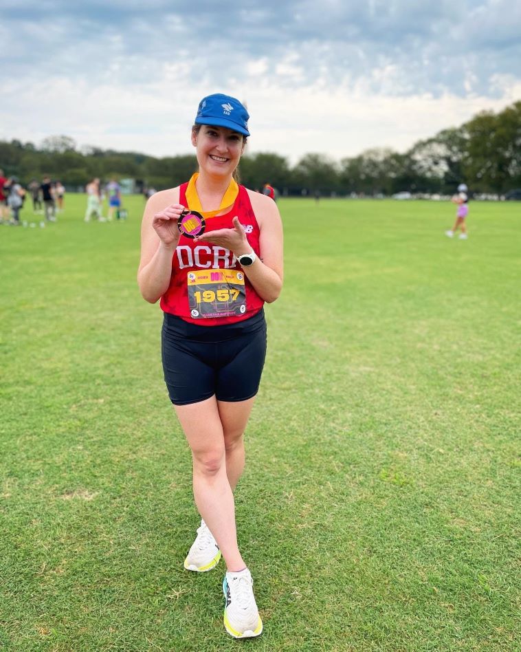 DC Road Runner Kristine Gift holding a finisher medal from the DC Half while standing on the grass in West Potomac Park
