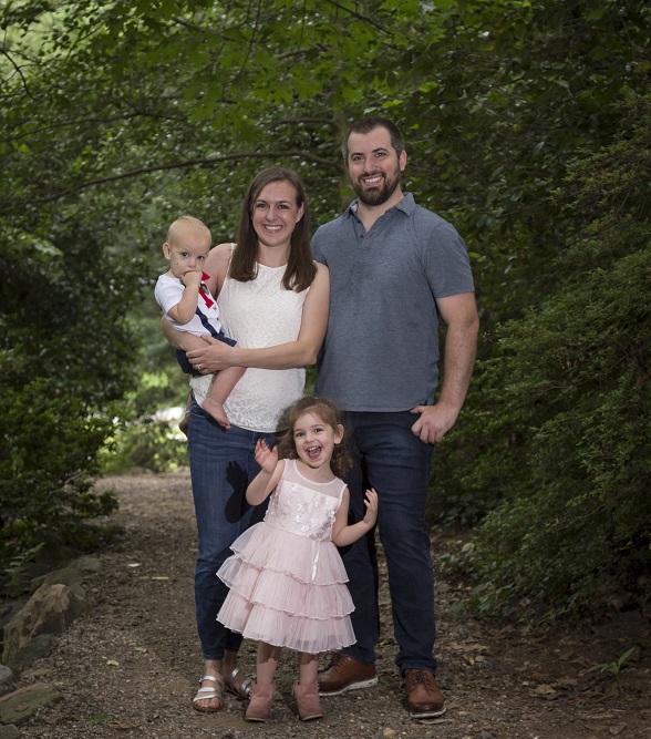 Lauren Firey standing for a posed with her husband and two children on a trail in the woods. They are wearing casual clothes and are not hiking.