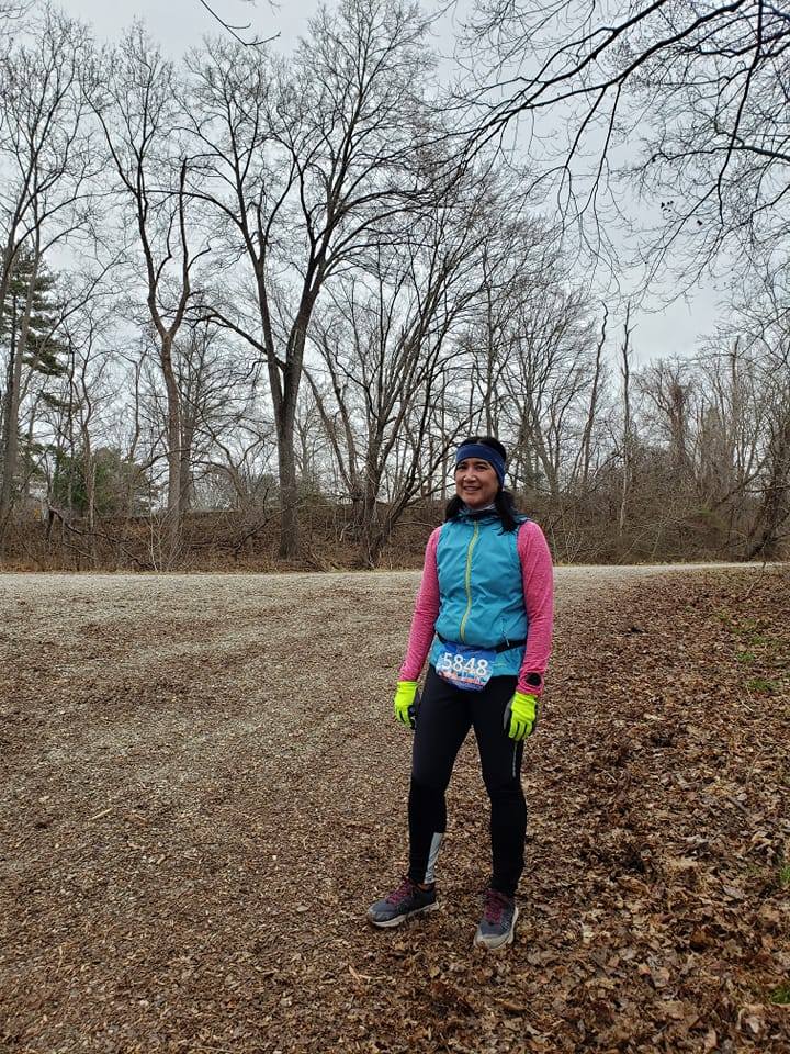 Ruby Len standing on a dirt trail wearing bright multicolored running gear and wearing a DC Road Runners race number