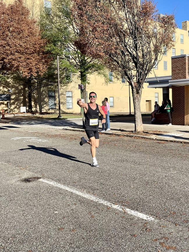 Steve Klug racing on a paved city street while pointing and smiling at the camera