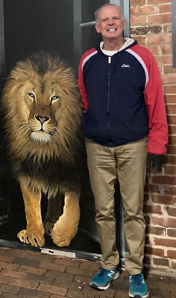 Ben Richter standing next to a convincingly life-like painting of a lion that could also maybe be a real lion