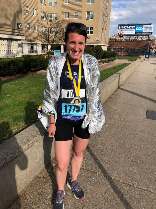 Hope Seck standing on a Boston sidewalk with a Boston Marathon finisher medal while wearing a navy blue DC Road Runners singlet