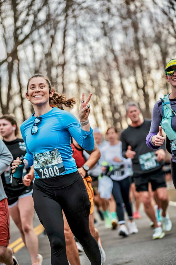 Lenise Phillips smiling and throwing a peace sign while running in a road race