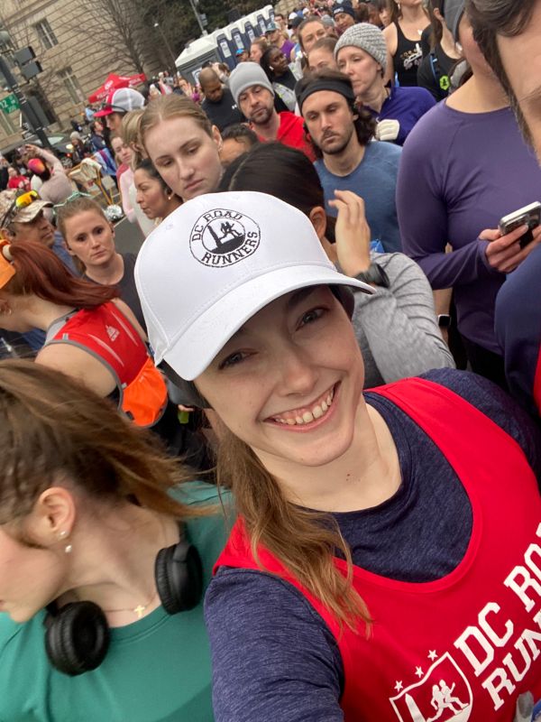 Rae Bimmerle wearing a red DC Road Runners singlet taking a selfie in a crowd of runners at the start of a race