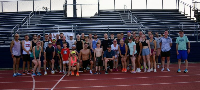participants in the 2025 DC Road Runners Global Running Day Mile Time Trial standing in a group on the Washington-Liberty High School track in front of metal bleachers