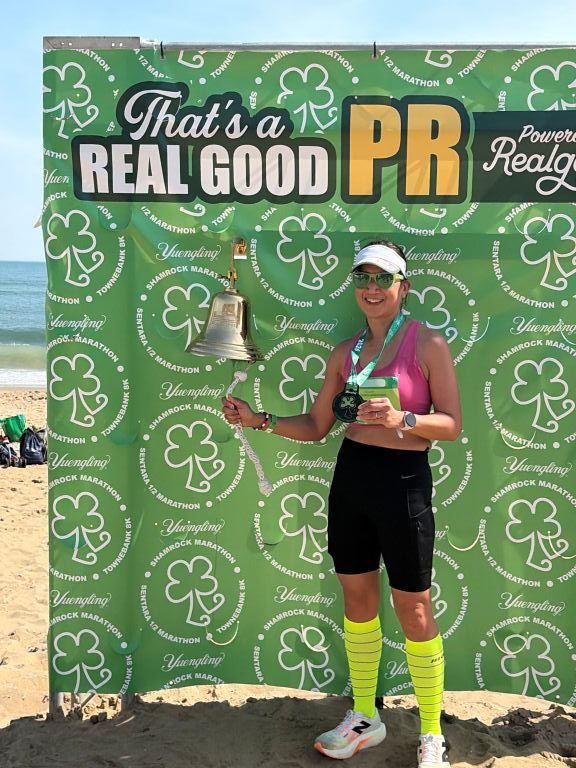 Ruby Len standing on the Virginia Beach sand, ringing a gold bell to acknowledge her new marathon PR