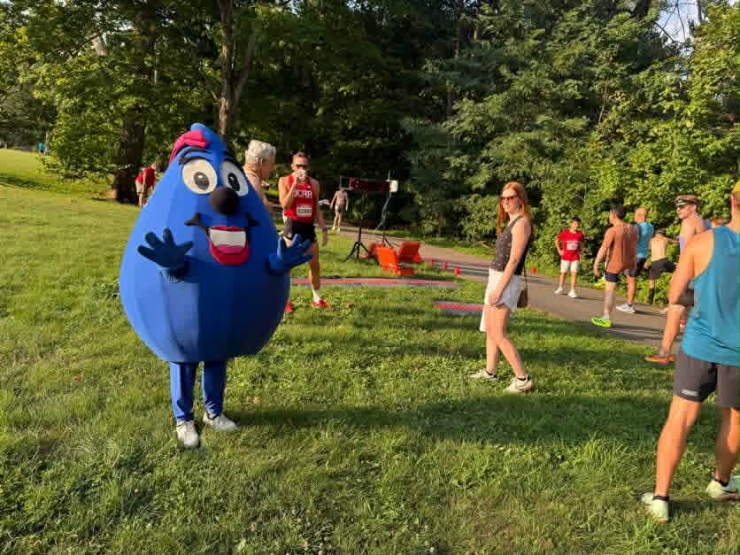 Wendy the Water Drop, the DC Water mascot, standing at the starting line of the 2026 Bluemont 5K with DC Road Runners members and race spectators